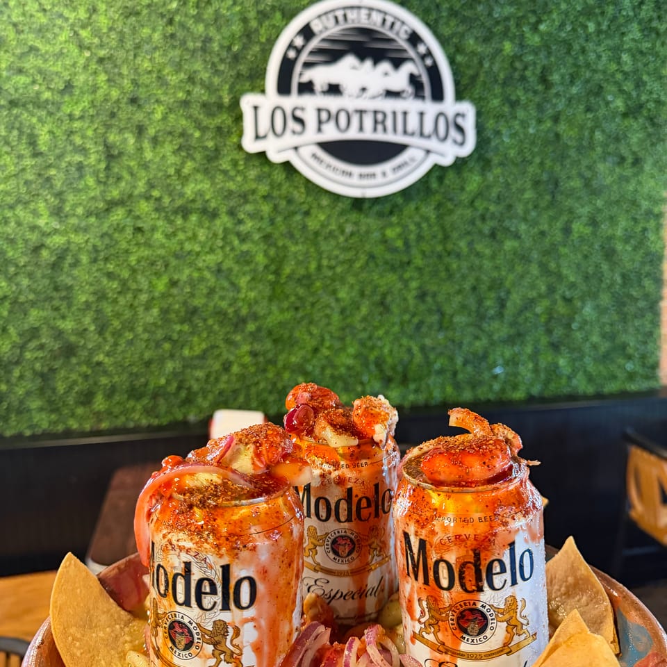 Three Modelo Especial beer cans topped with shrimp and garnishes, surrounded by tortilla chips, beneath the Los Potrillos logo.