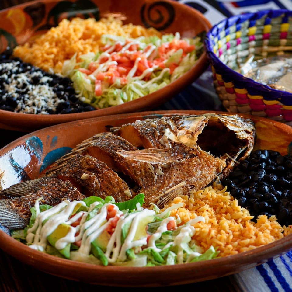 Traditional Mexican platters featuring whole fried fish, rice, black beans, lettuce, tomatoes, and colorful woven textiles.