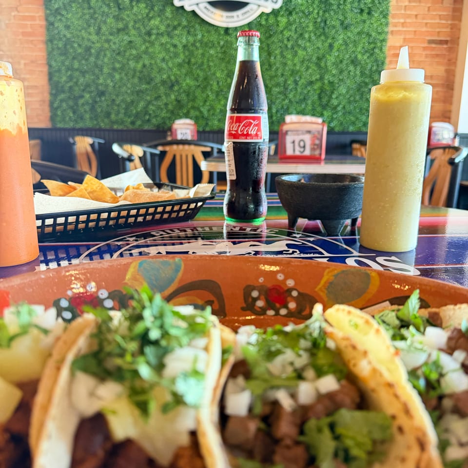 Tacos with cilantro, onions, lime, chips, salsa, Coca-Cola, and sauces at Los Potrillos Mexican restaurant.
