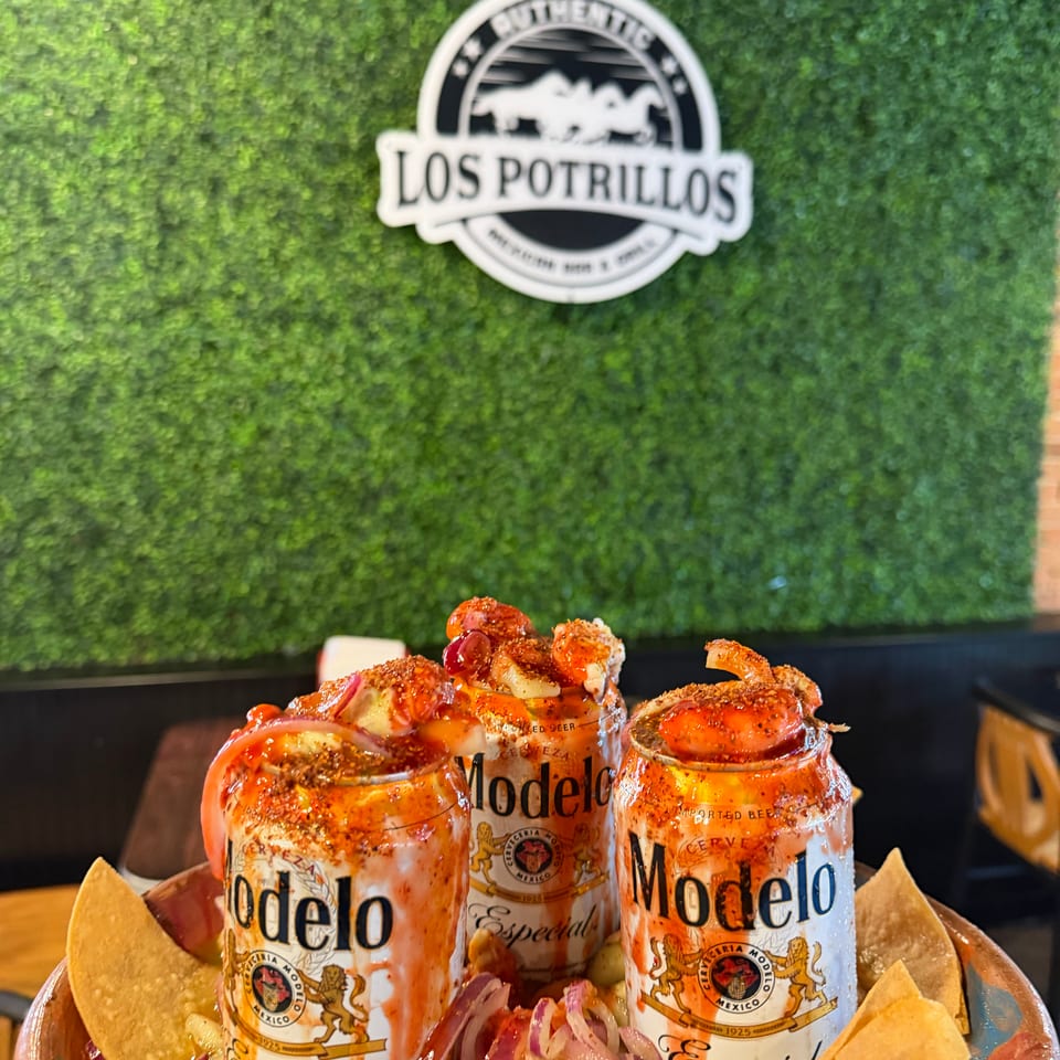 Three shrimp-topped micheladas with vegetables and tortilla chips sit beneath the Los Potrillos restaurant logo.